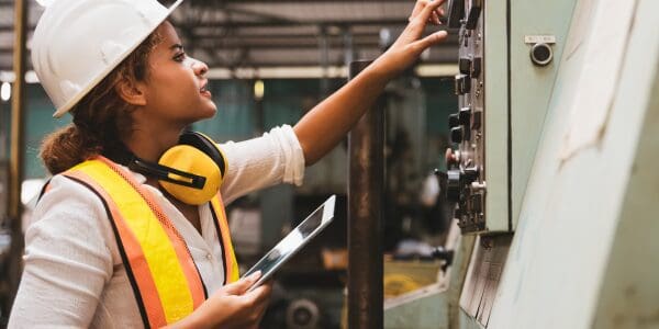 Woman is pictured with hands operating a machine and holding a tablet device